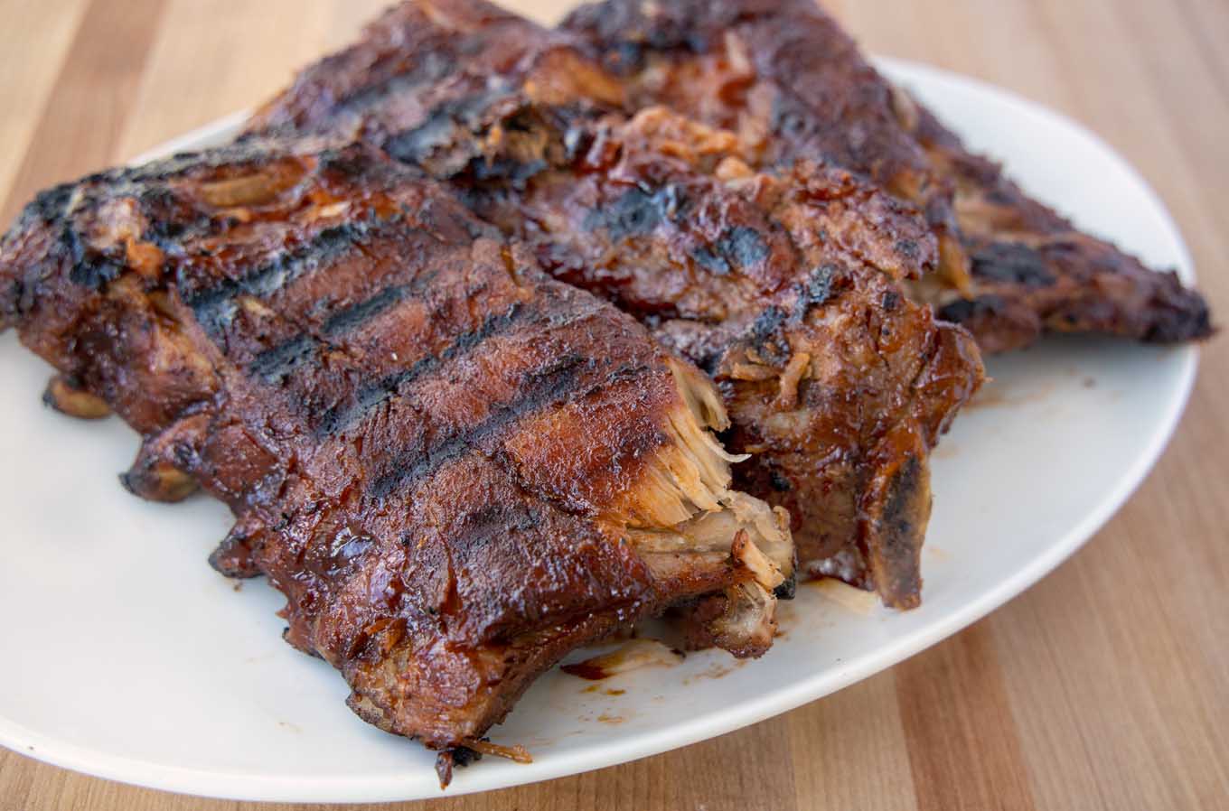 3 half racks of grilled baby back ribs on a white platter