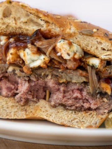 view of Cheeseburger cut in half with pulled pork, barbecue sauce and bleu cheese on a white plate