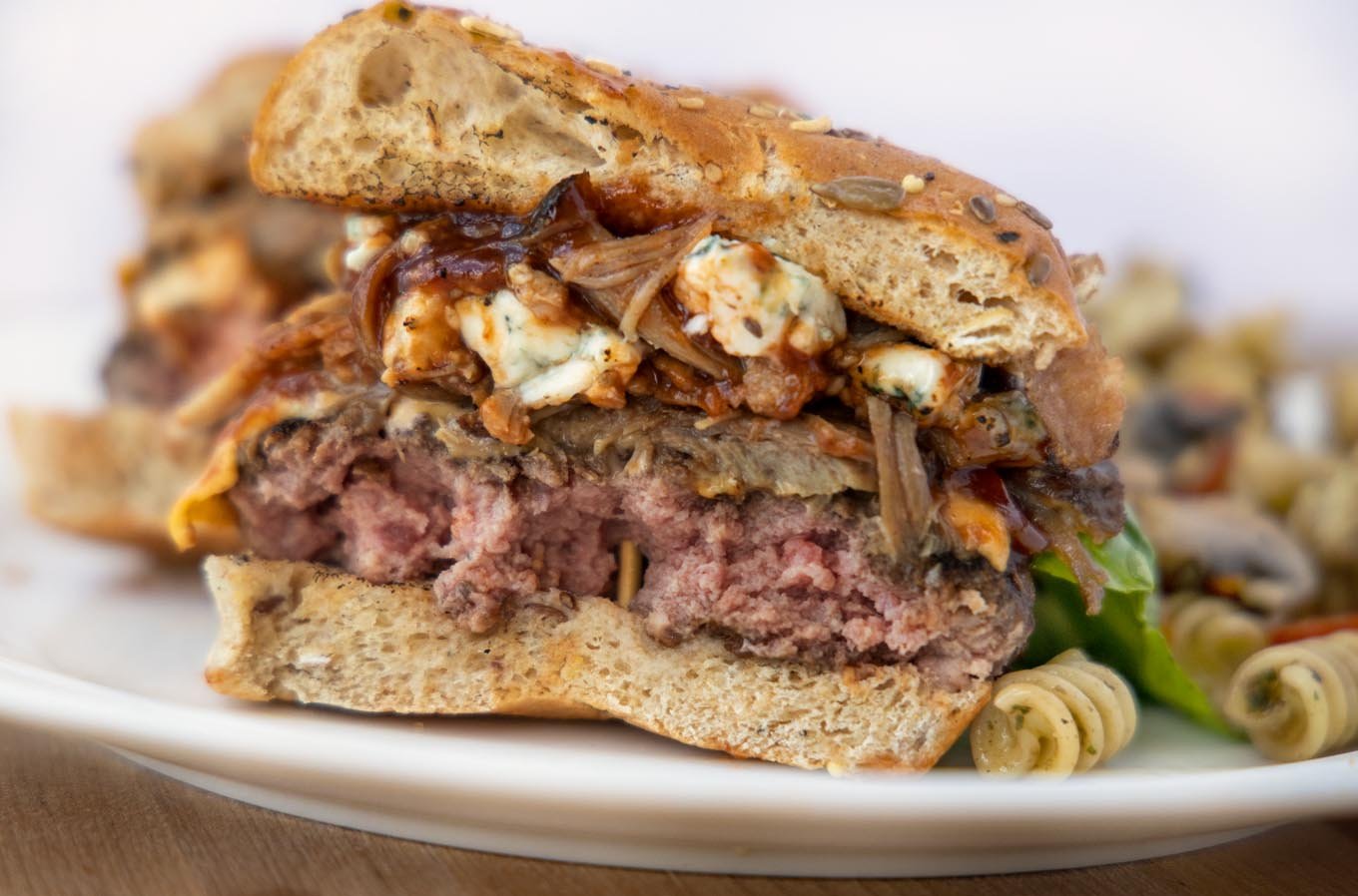 view of Cheeseburger cut in half with pulled pork, barbecue sauce and bleu cheese on a white plate