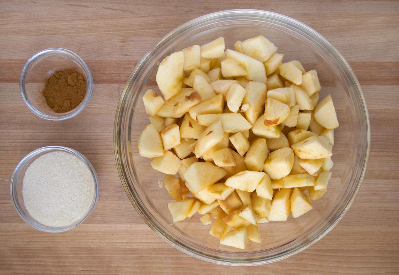 apples, sugar and cinnamon in bowls on a wooden cutting board