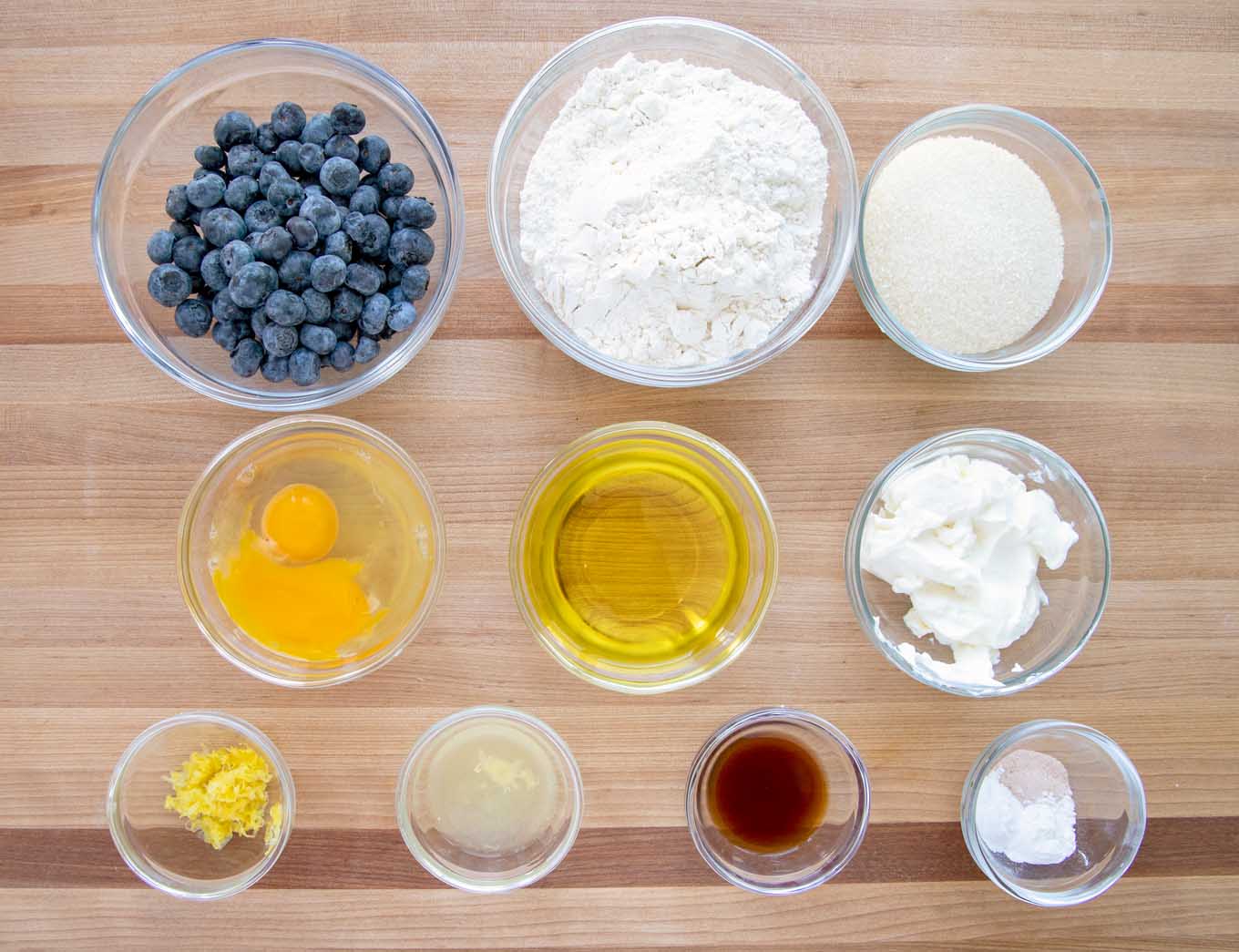 ingredients to make blueberry muffins in glass bowls on a wooden cutting board