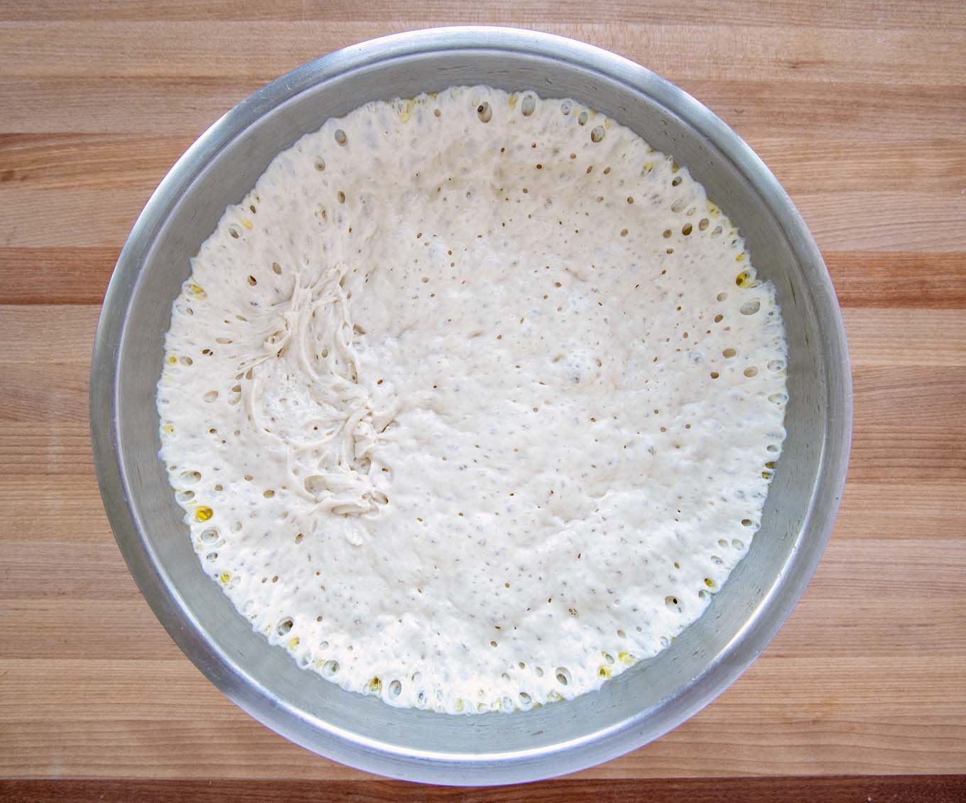 bread dough in a metal bowl,  with bubbles after the first rise