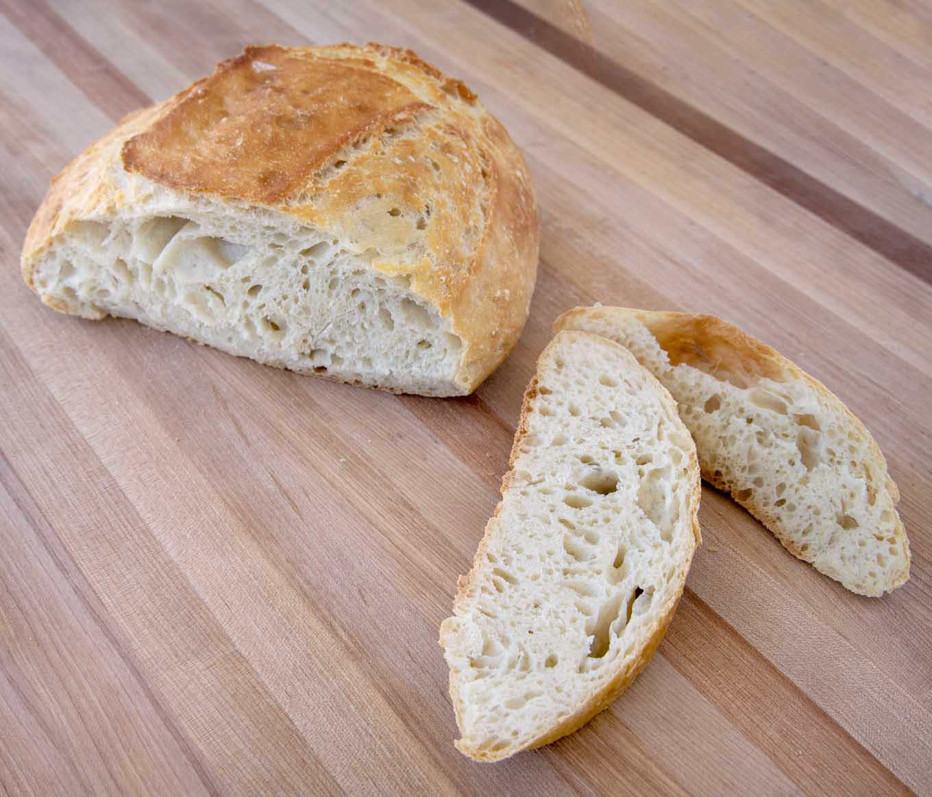 loaf of artisan bread sliced with slices next to it on a wooden cutting board