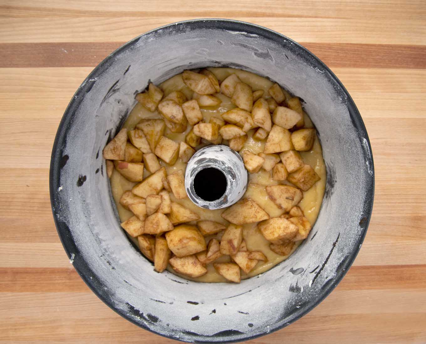 overhead view of a small layer of  cake batter topped with apples in a floured ring cake pan