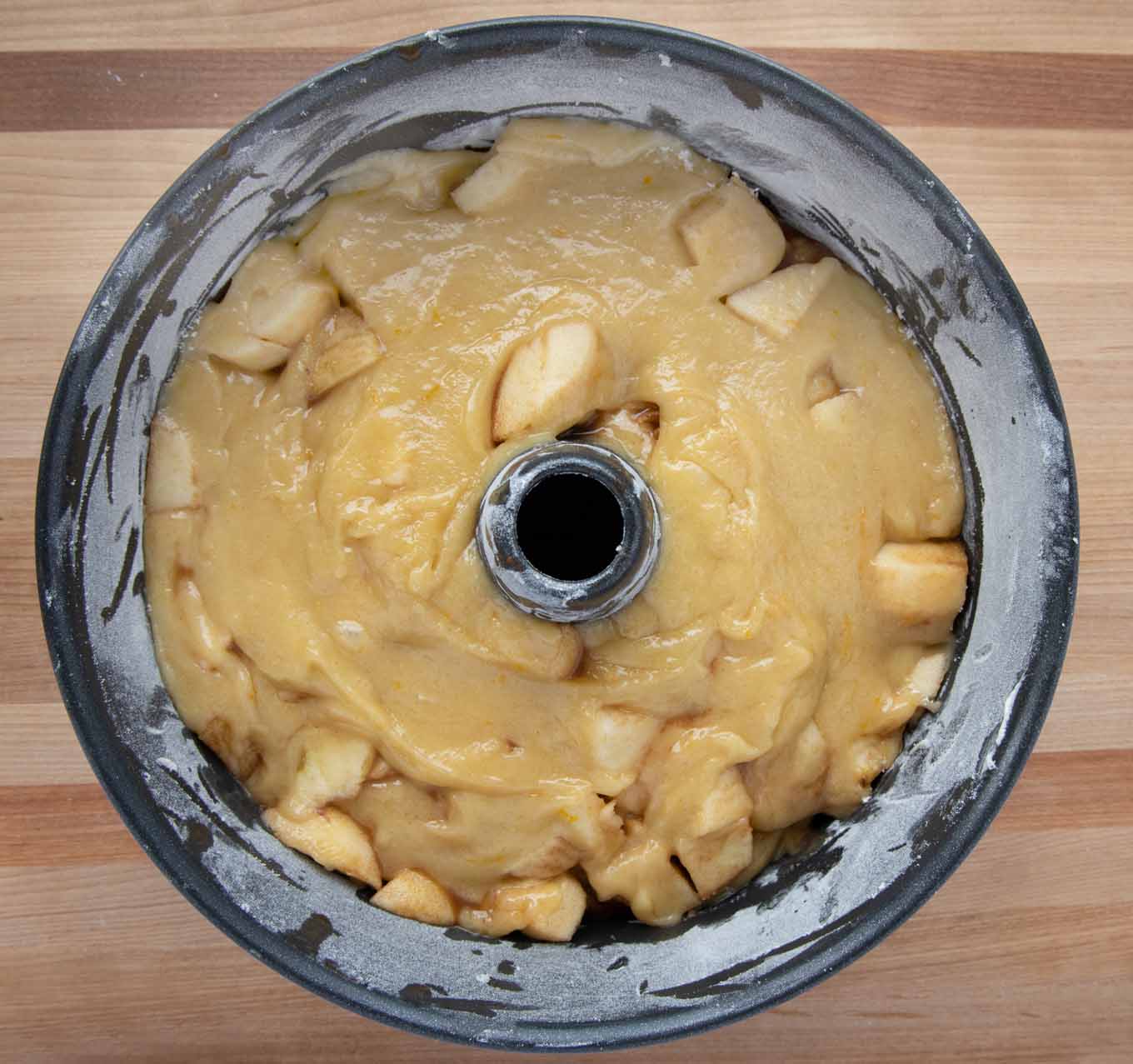ring pan full of cake batter and apples that have been layered in the pan