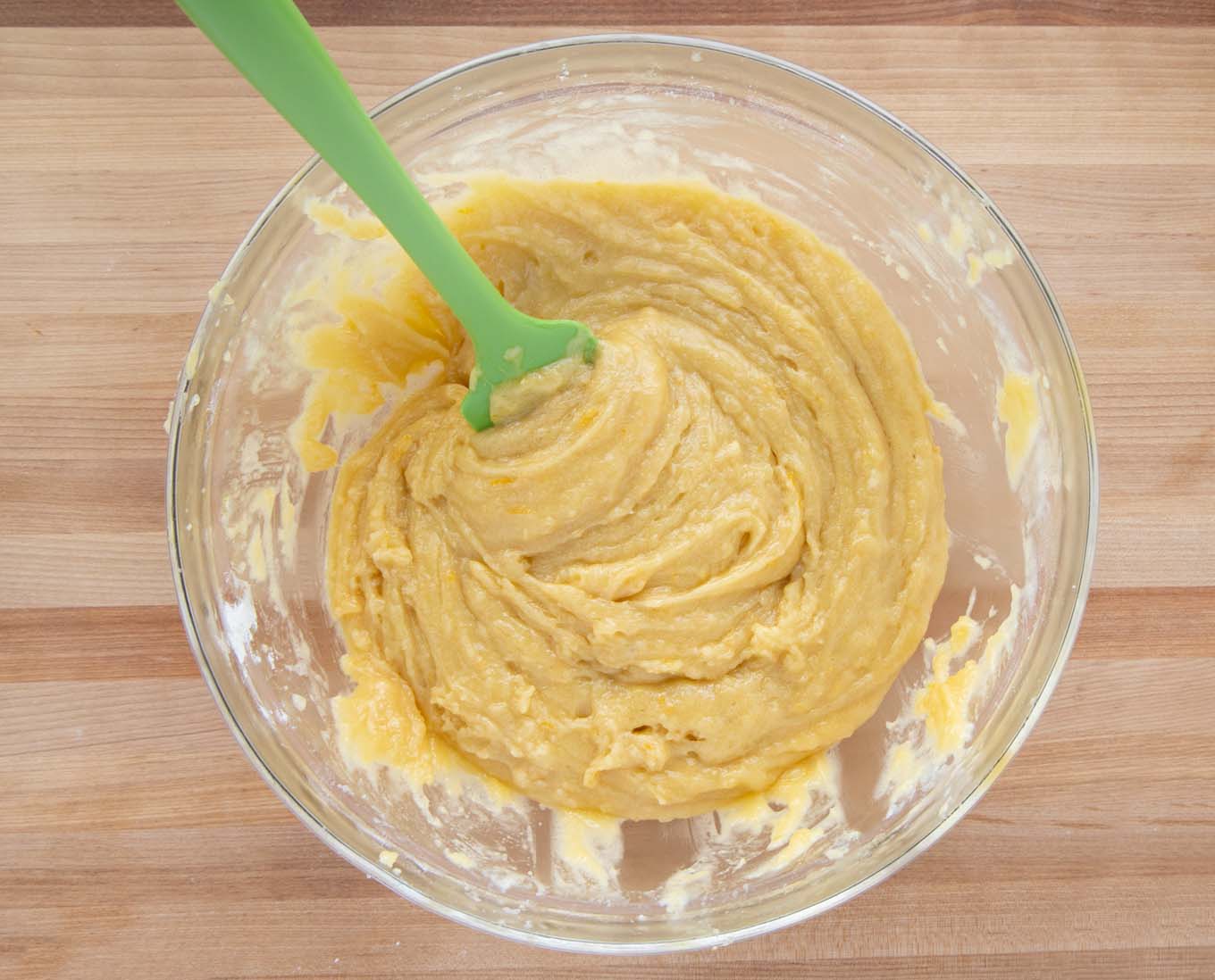 overhead view of the cake batter in a glass bowl with a green rubber spatula after the eggs have been added