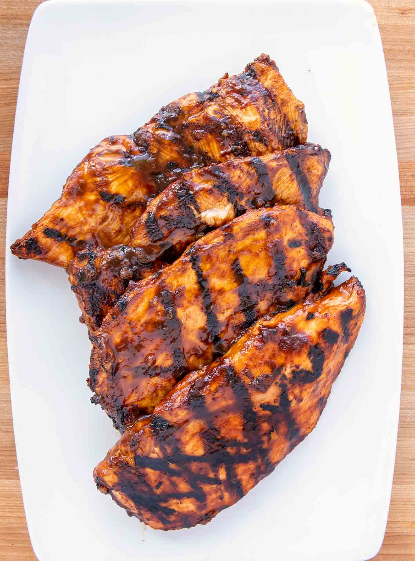 4 grilled barbecued chicken breasts with grill marks on a white platter