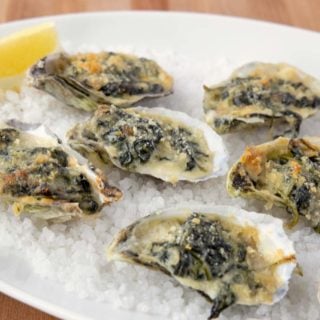 oysters rockefeller with a slice of lemon on a bed of rock salt on a white platter
