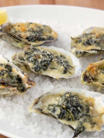 oysters rockefeller with a slice of lemon on a bed of rock salt on a white platter