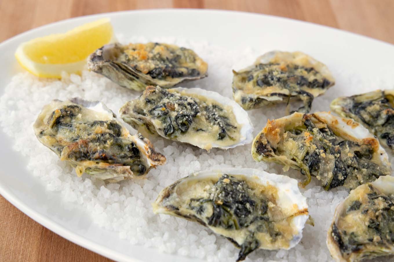 oysters rockefeller with a slice of lemon on a bed of rock salt on a white platter