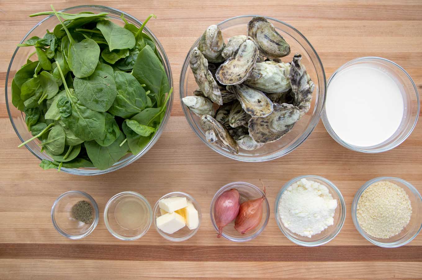 ingredients to make Oysters Rockefeller in glass bowls on a wooden cutting board