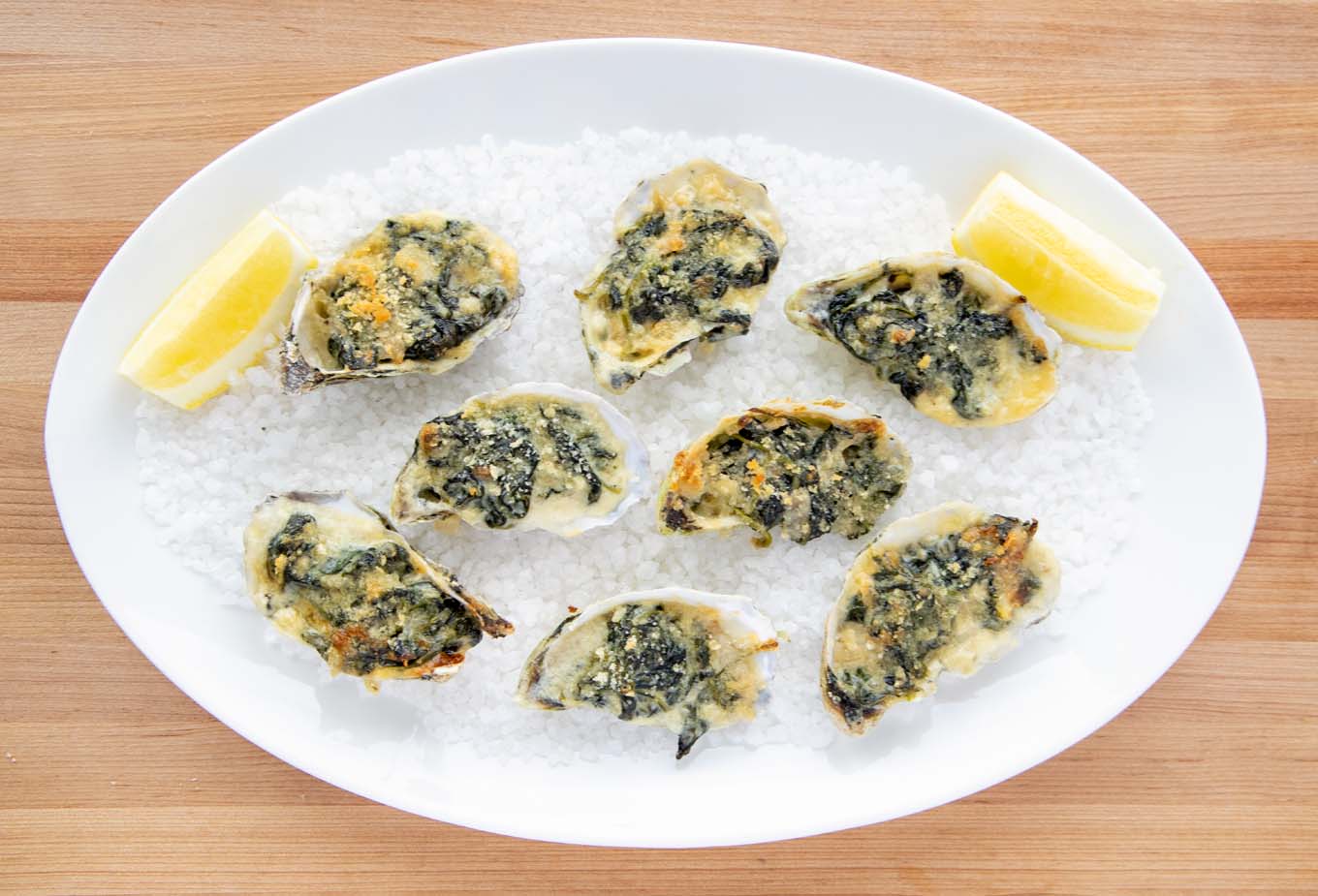 8 oysters rockefeller on a bed of rock salt with lemon slices  white oval platter