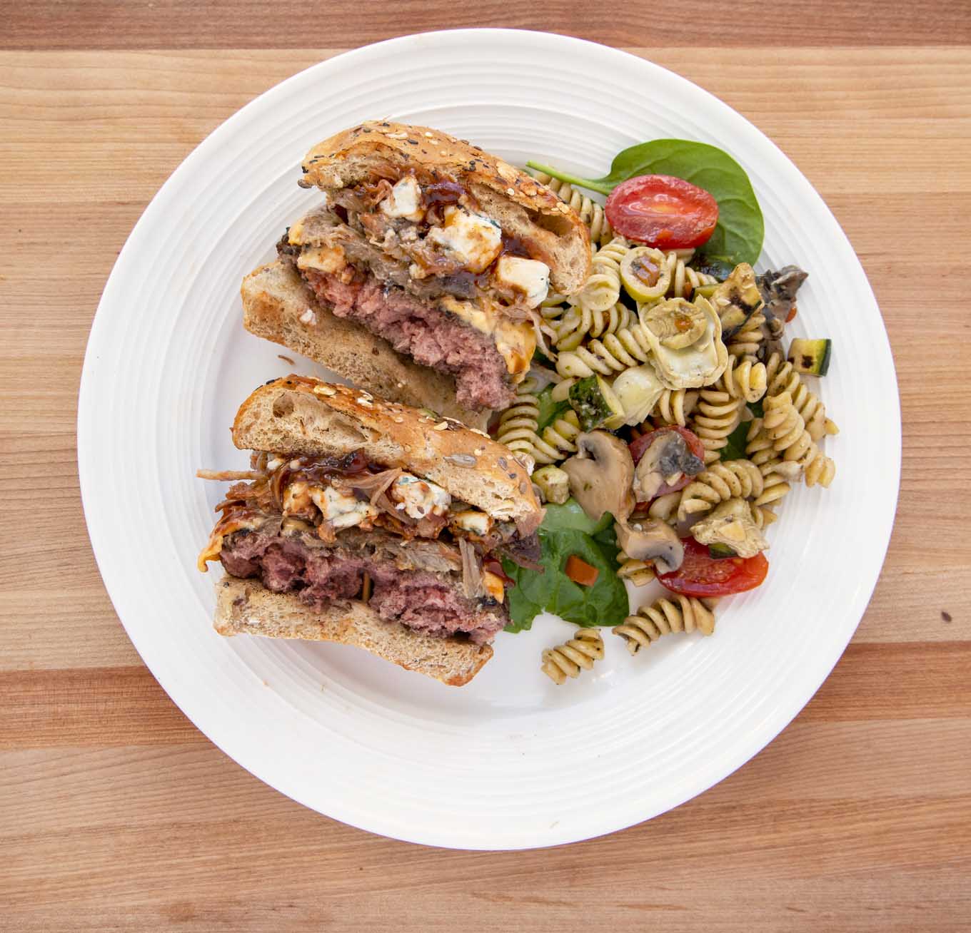 Pulled Pork Cheeseburger on a seeded bun cut in half with pasta salad on a bed of spinach on a white plate