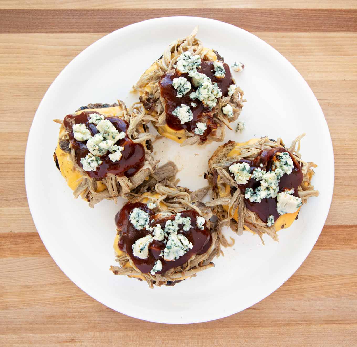 4 Cheeseburgers topped with pulled pork, barbecue sauce and bleu cheese crumbles on a white platter