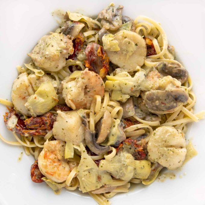 overhead shot of Seafood Riviera consisting of shrimp, scallops mushrooms, sun-dried tomatoes and sliced artichoke hearts in a pesto sauce served over linguine