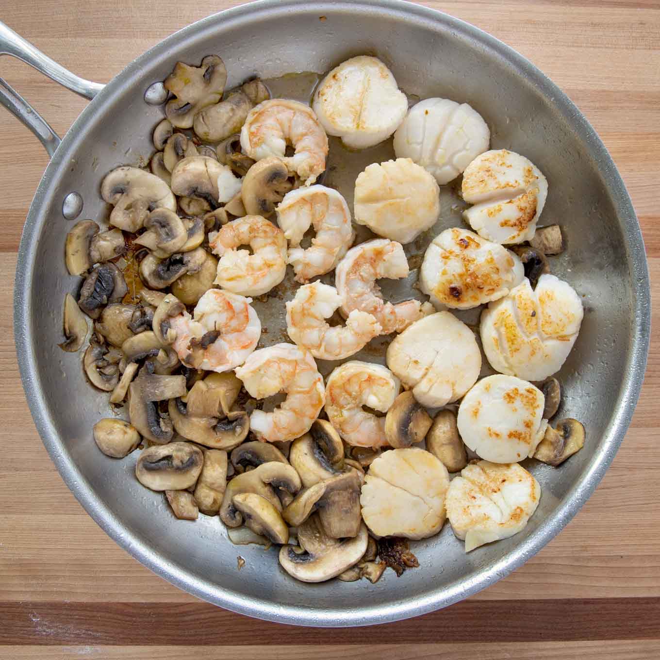 ingredients to make seafood riviera including scallops, shrimp and mushrooms in a large saute pan
