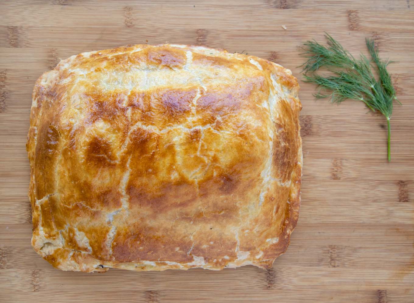 Baked Coulibiac of Salmon with a sprig of dill on a wooden cutting board