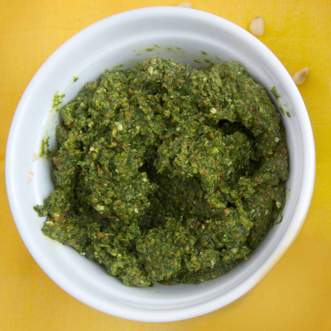 white bowl of basil pesto on a yellow table cloth