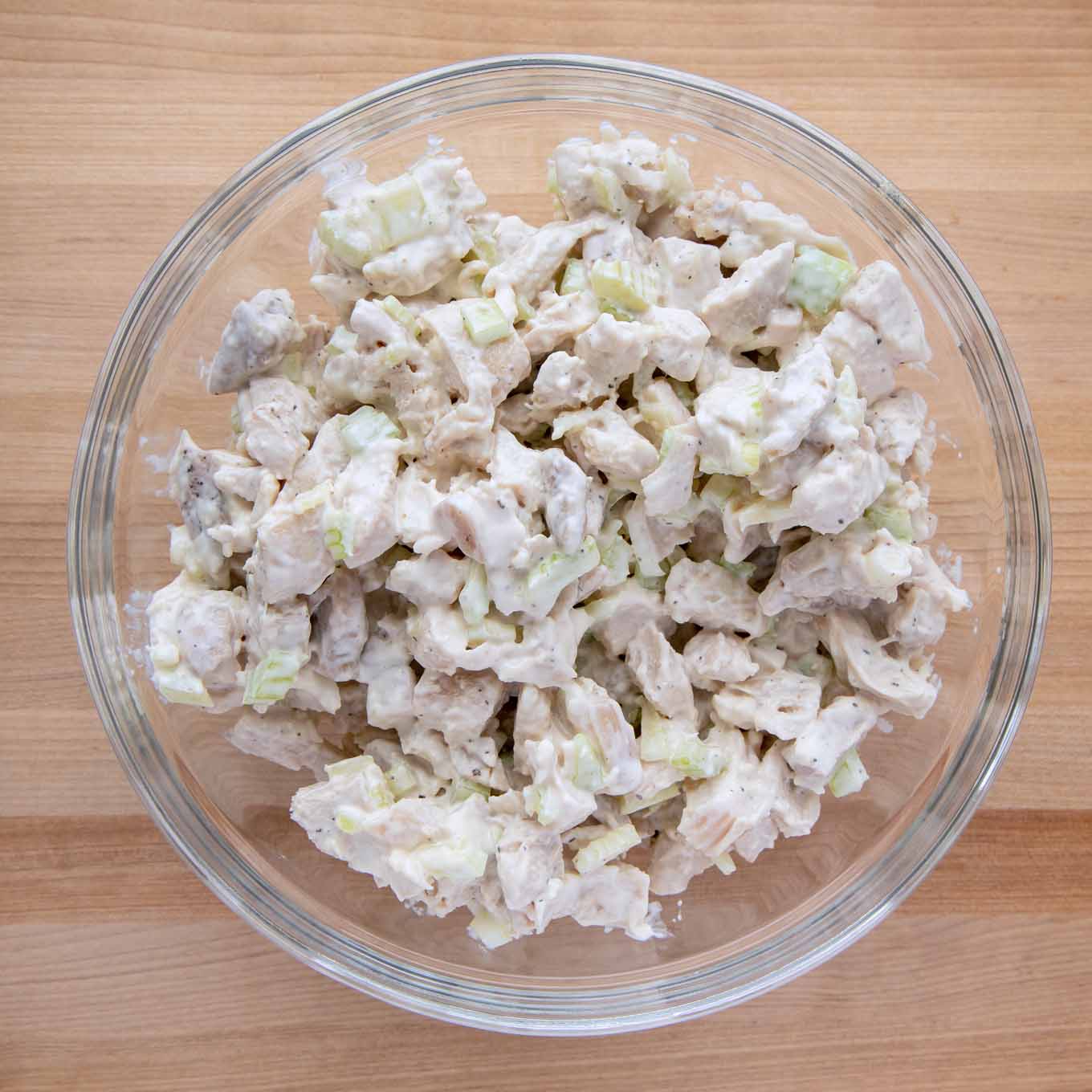 overhead view of chicken salad in a glass bowl on a wooden cutting board