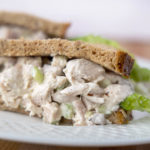 half of a chicken salad sandwich with lettuce on grain bread on a white plate