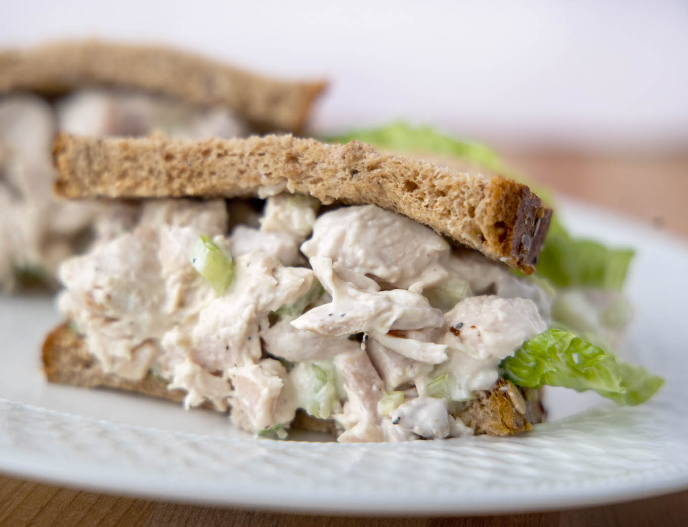 half of a chicken salad sandwich with lettuce on grain bread on a white plate