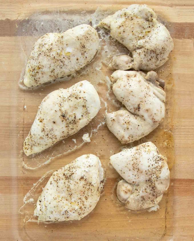 cooked seasoned boneless, skinless chicken breasts and thighs in a glass baking dish on a wooden cutting board