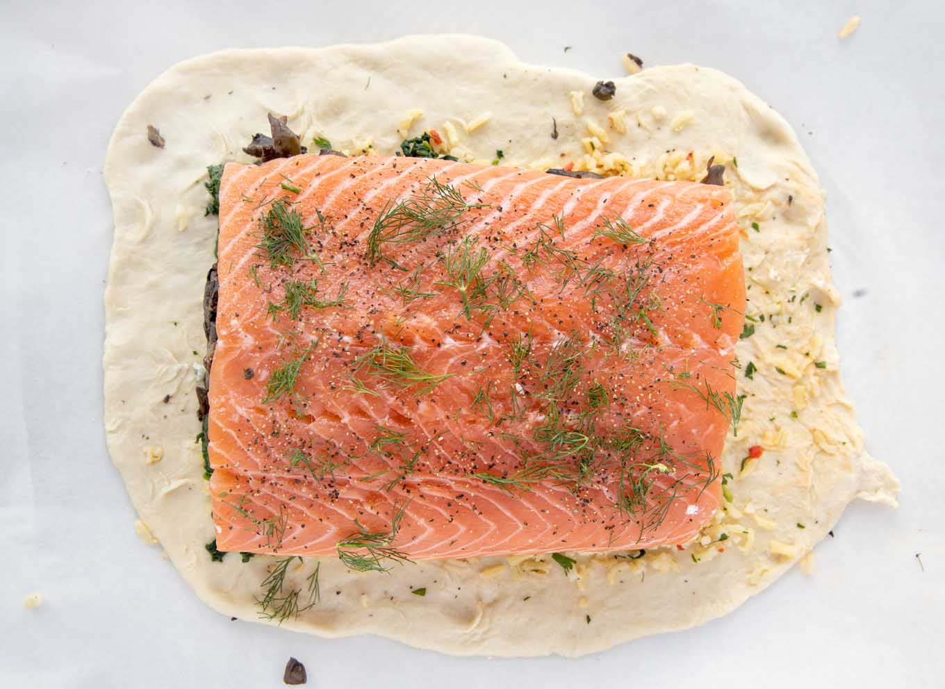 overhead view of salmon seasoned with sea salt, pepper and dill on puff pastry sheet
