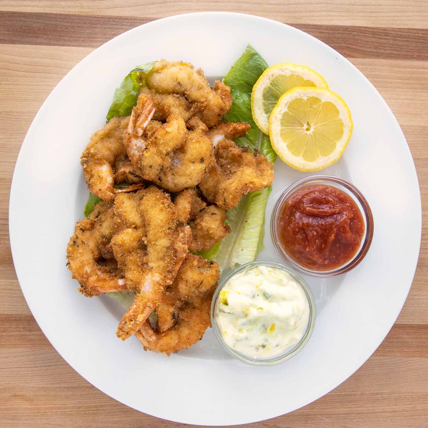 overhead view of golden brown fried shrimp on a white plate with tarter sauce, cocktail sauce and lemon slices