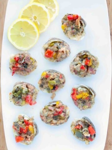 Clams Casino on a white platter with lemons.