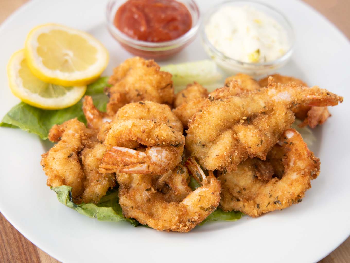 golden brown fried shrimp on a white plate with tartar sauce, cocktail sauce and lemon slices