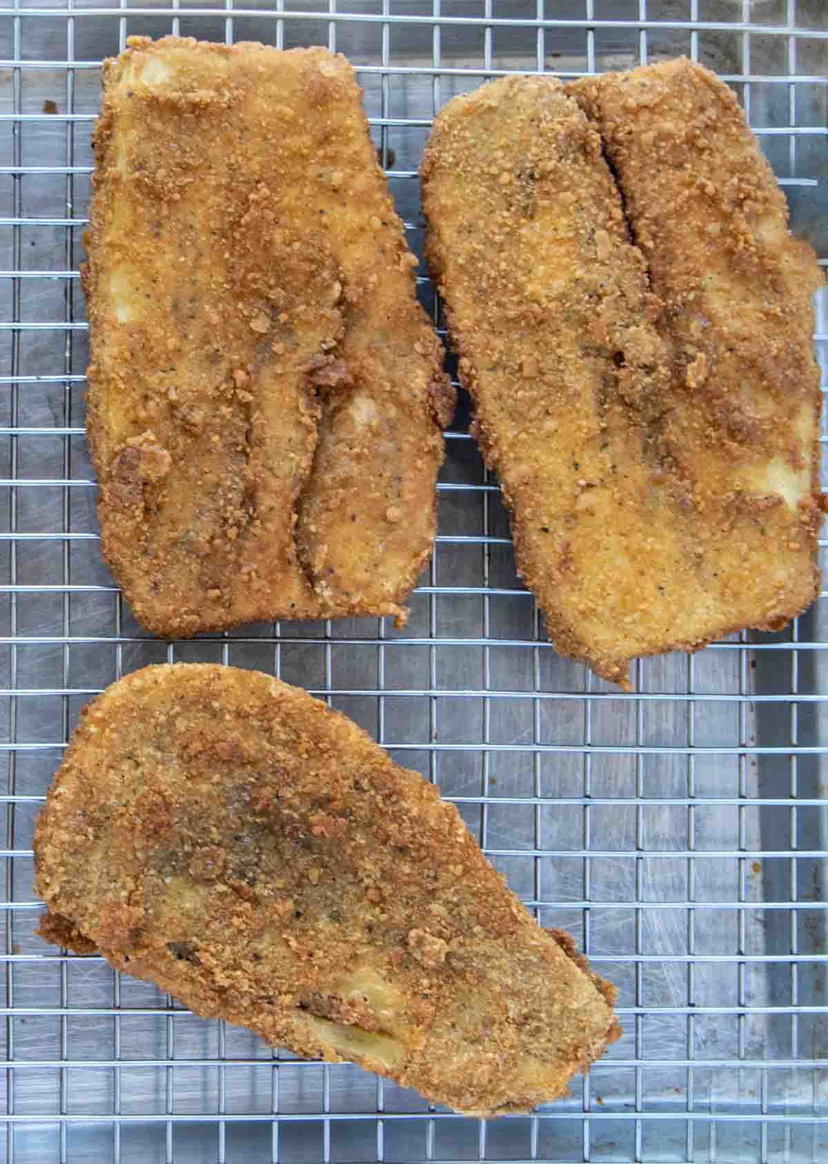 fried eggplant cutlets draining on a screen over a sheet pan