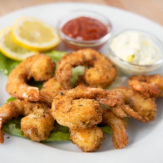 golden brown fried shrimp on a white plate with tarter sauce, cocktail sauce and lemon slices