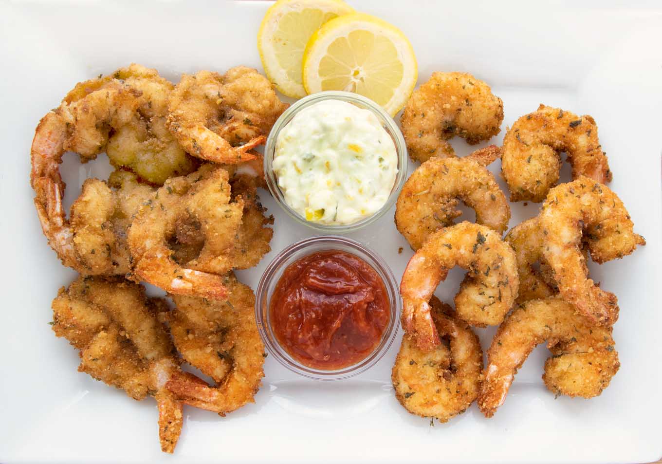 fried butterfly shrimp and fried regular shrimp on a white platter with tartar sauce, cocktail sauce and lemon slices