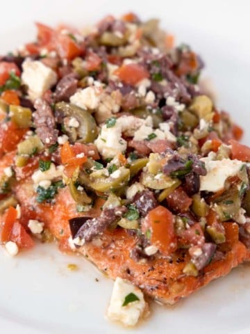 roasted salmon fillet topped with feta olive tapenade on a white plate