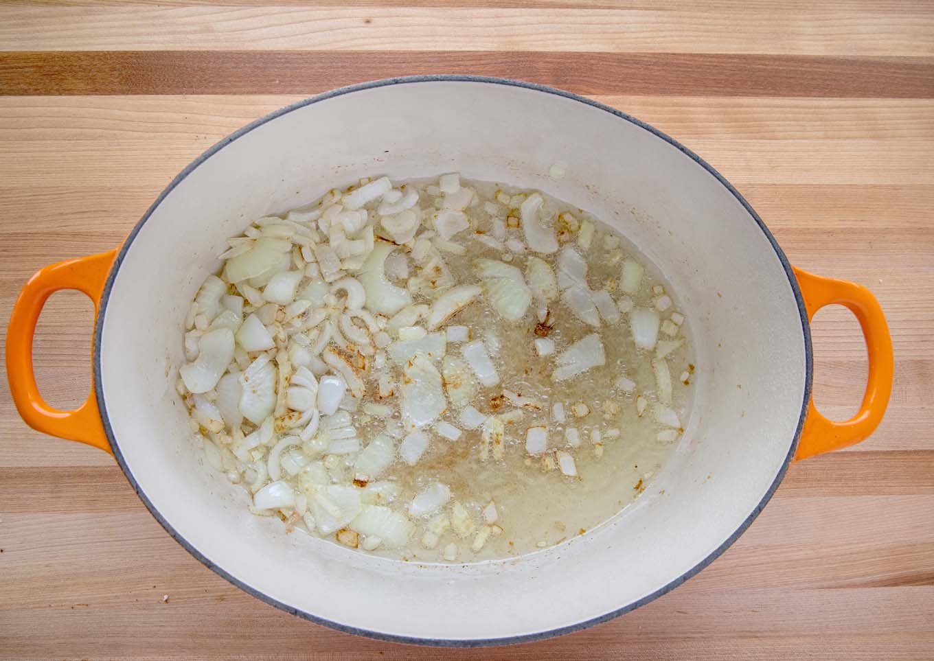 chopped onions in oil in a dutch oven sitting on a cutting board