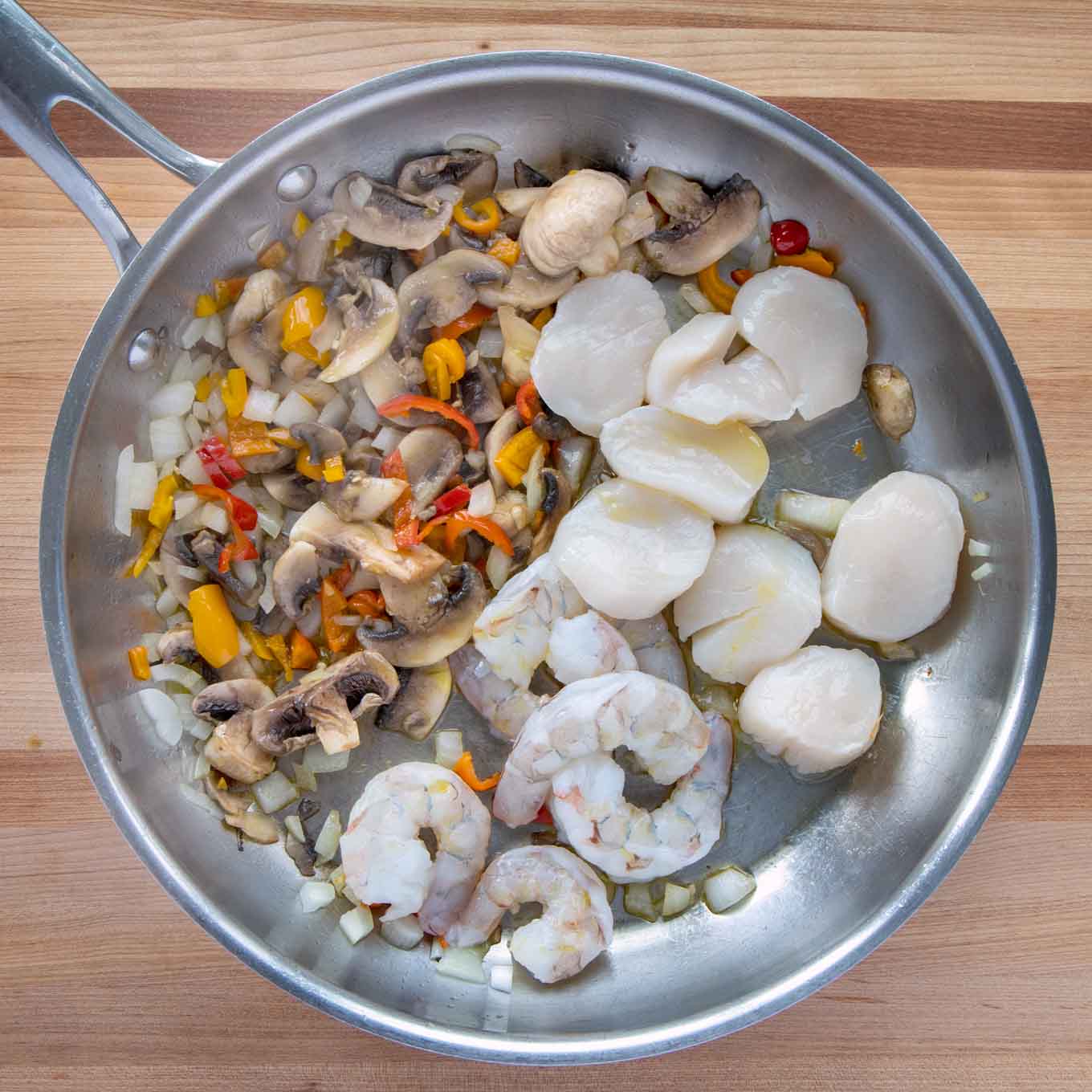 peppers, onions, mushroom, shrimp and scallops in a frying pan