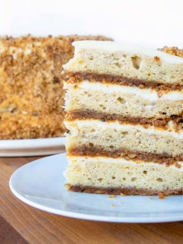 slice of banana crunch cake on a white plate in front of the whole cake