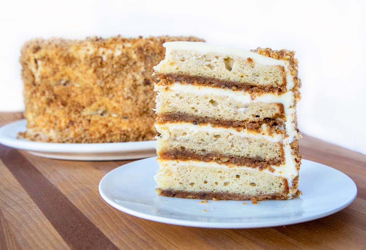 slice of banana crunch cake on a white plate in front of whole cake