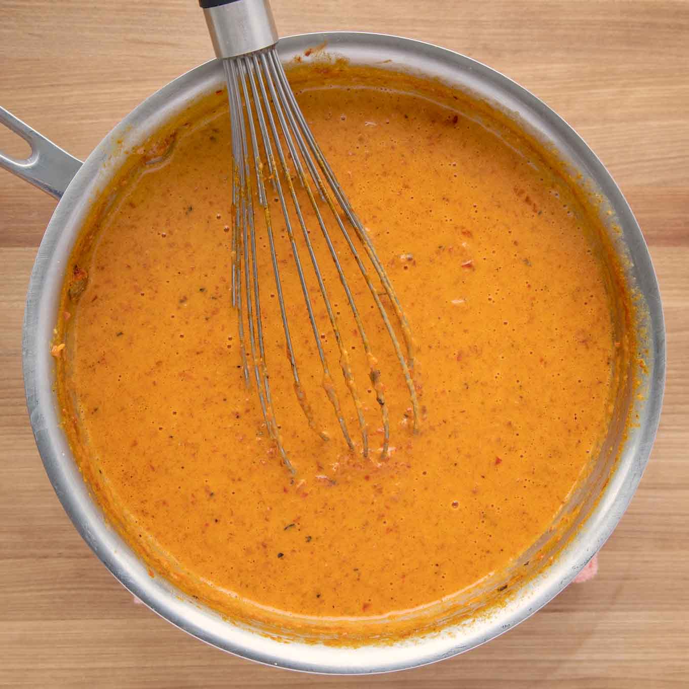 cooked roasted red pepper sauce in a sauce pan with a wire whisk