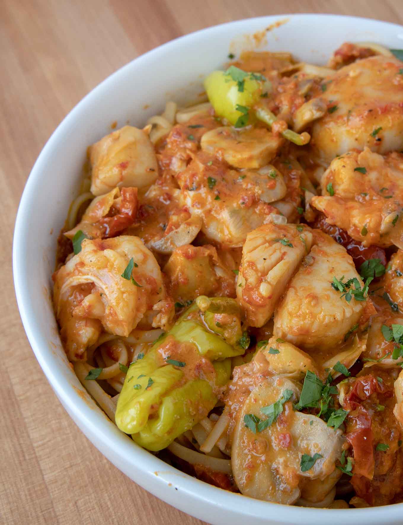 partial view of shrimp and scallops in a roasted red pepper sauce served over linguine in a white bowl