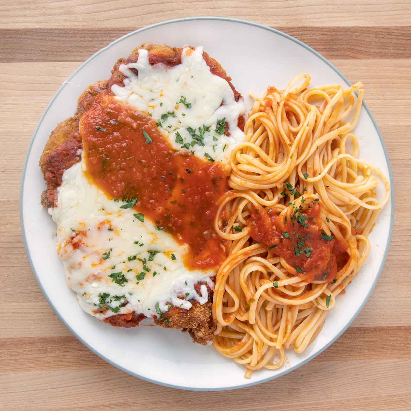 Chicken parmesan with linguine on a white plate.