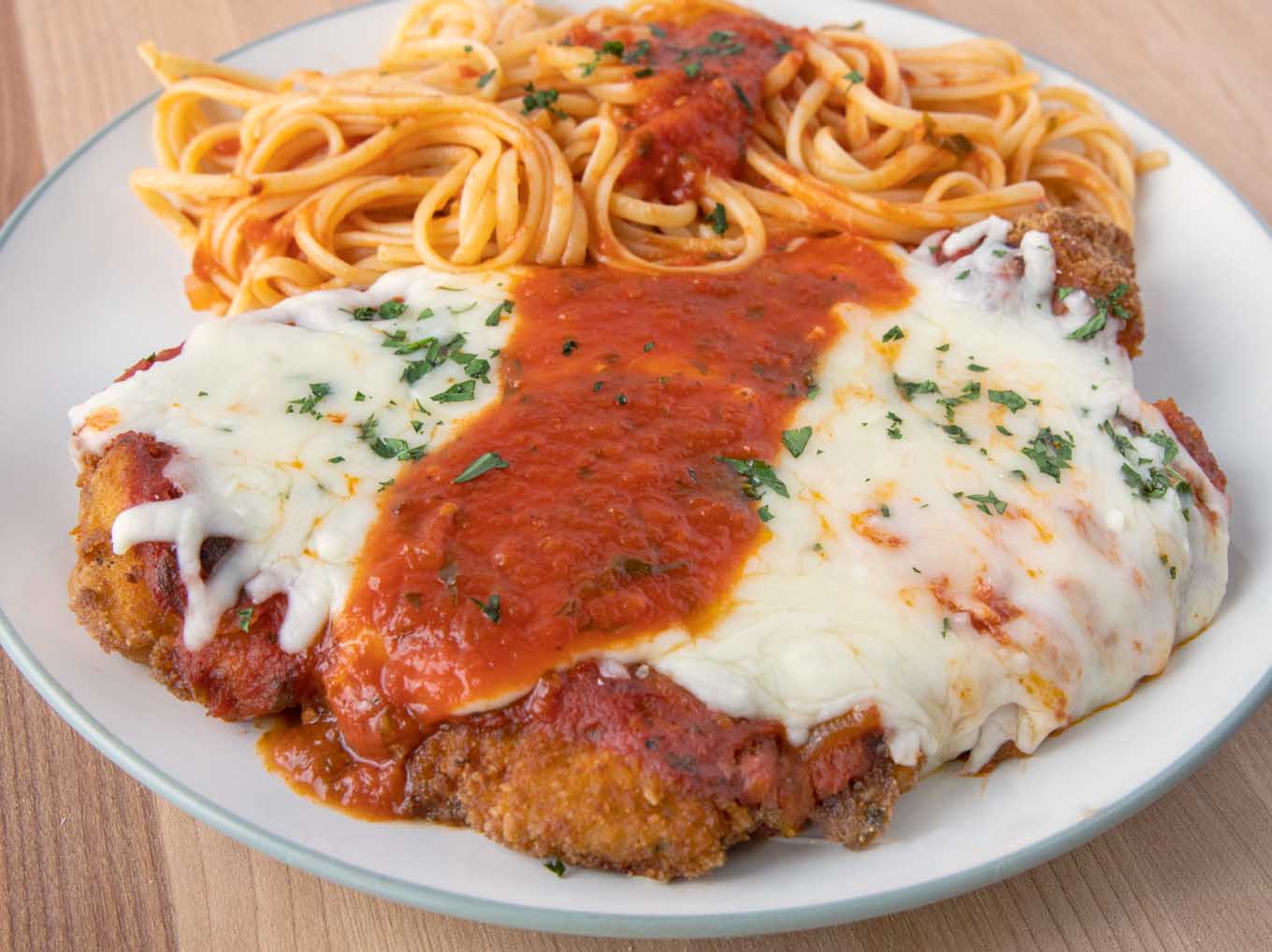 chicken parmesan and pasta on a green rimmed white plate.