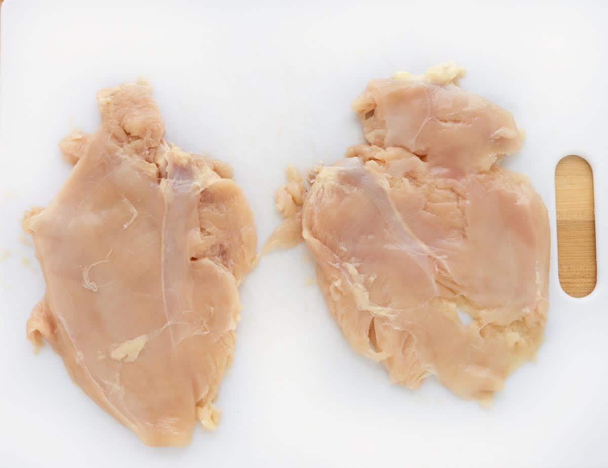 Chicken breasts pounded flat on cutting board.