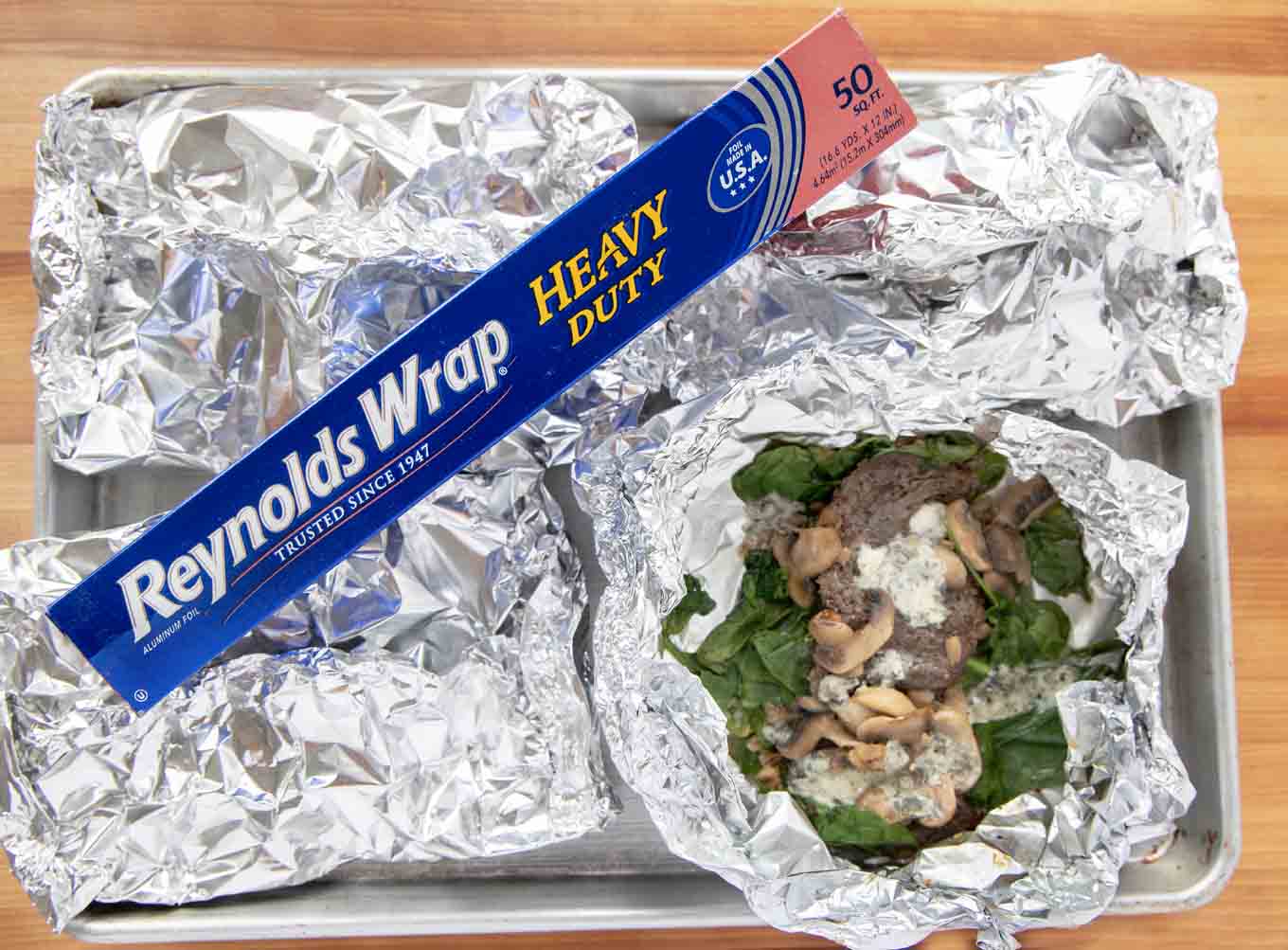 4 foil packets with one open showing the finished skirt steak on a sheet pan with a box of Reynolds foil across on the top 