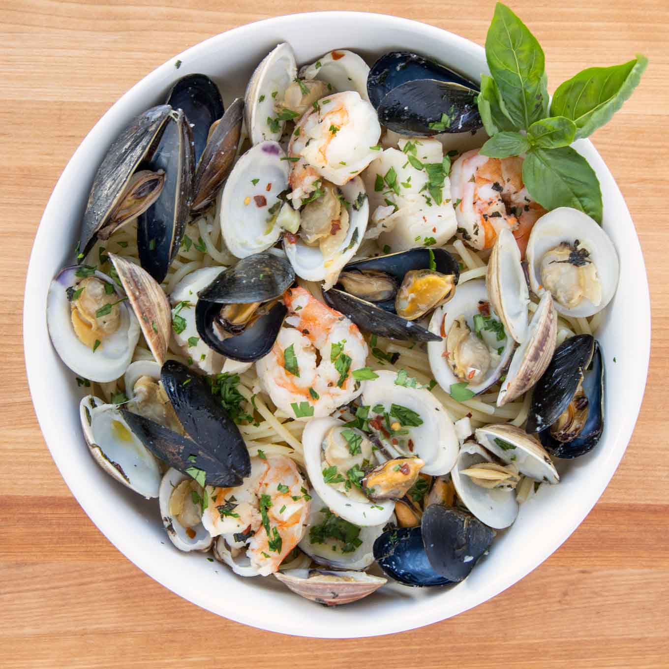 frutti di mare served over spaghetti with a sprig of basil in a white bowl