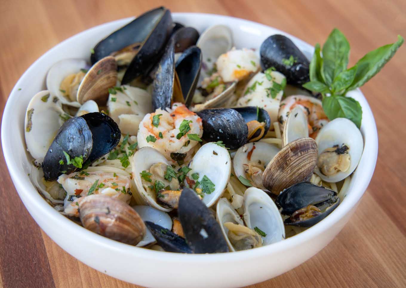 Frutta di mare served over spaghetti with a sprig of basil in a white bowl