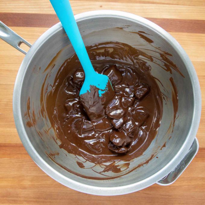 melting chocolate in a stainless steel bowl with a blue plastic spatula