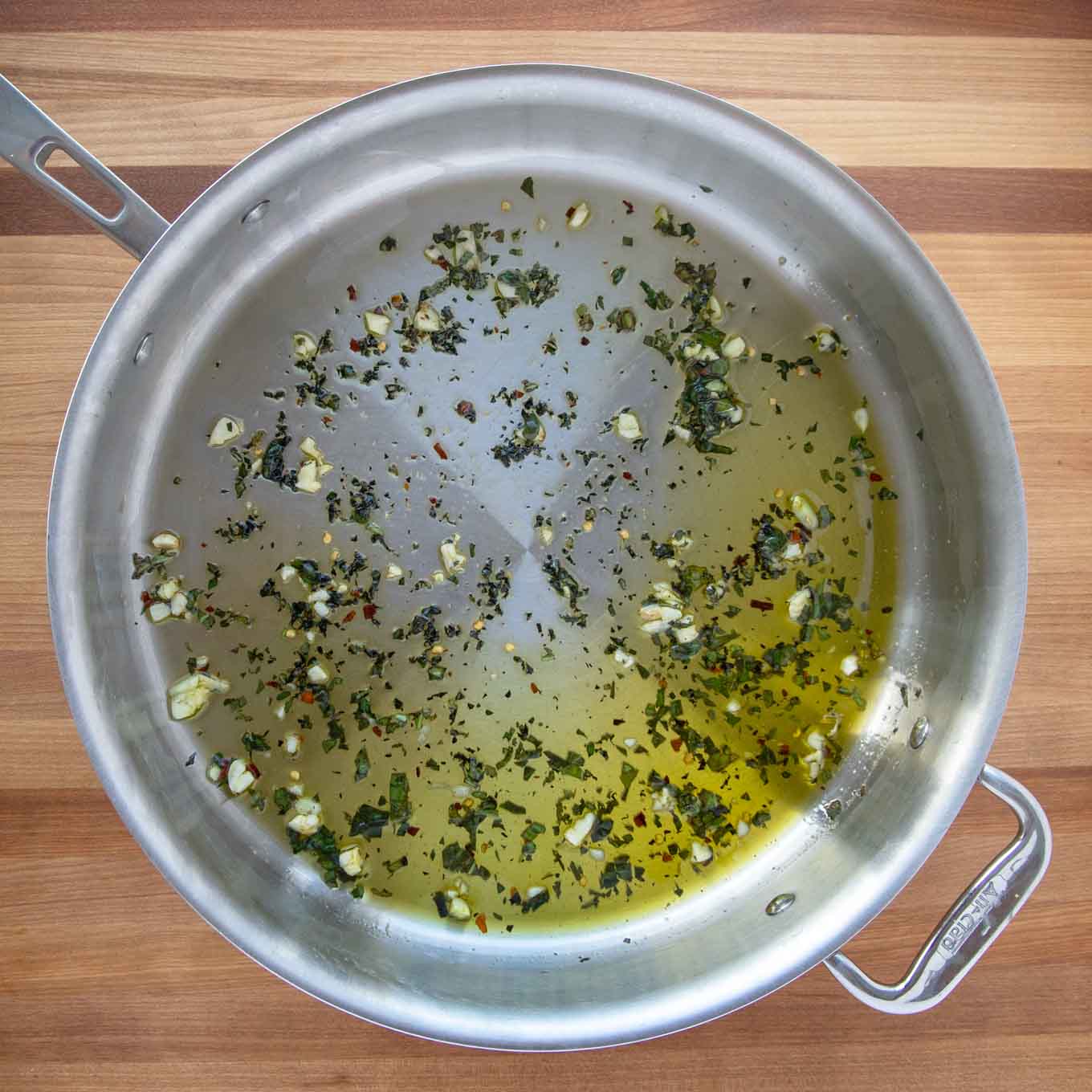 large saute pan with olive oil, garlic and chopped basil