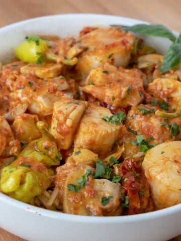 shrimp and scallops in a roasted red pepper sauce served over linguine in a white bowl