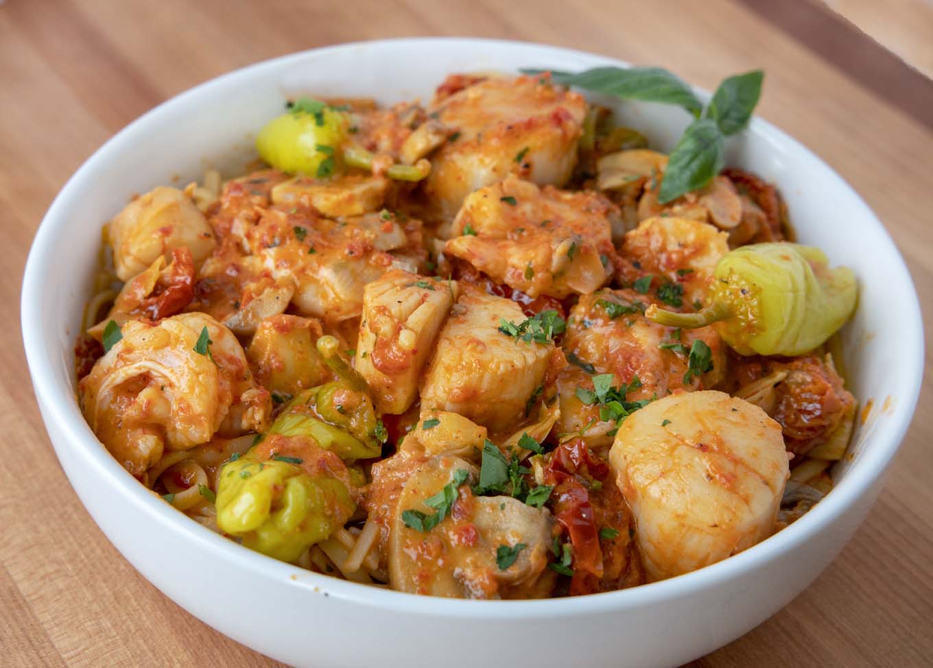 shrimp and scallops in a roasted red pepper sauce served over linguine in a white bowl